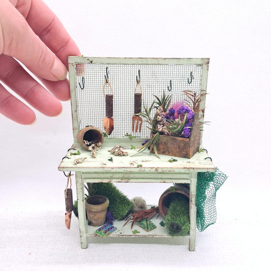 A 12th scale dolls house miniature potting bench complete with miniature plant pots, tools, turf rolls and dried flowers. 