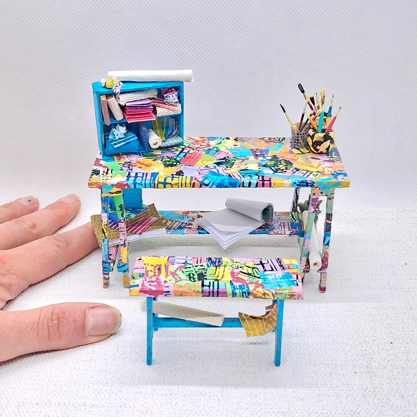 A colourful dolls house miniature artists desk and stool set handmade in the 12th scale. The desk is decoupaged with hand painted paper and fully topped with tiny artistic miniatures. 