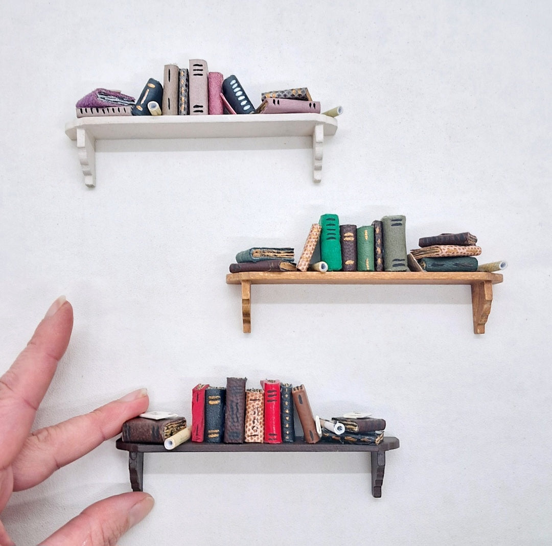 dolls house miniature book shelves with colourful leather  bound books and a hand holding one for scale purposes.