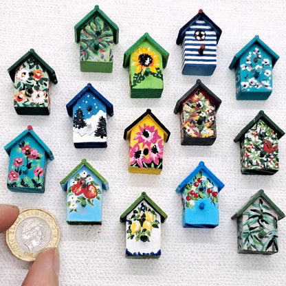 Miniature bird houses that are wooden and hand painted in colourful designs. a pound coin is shown next to them for scale.