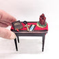 A 1/12th scale religious themed console table in dark red brown. The table is topped with a miniature bible, candles and religious icons 